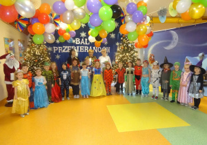 Pani dyrektor Maria Królikowska, p. Arleta, p. Ewa wraz z grupą przebranych dzieci stoi na tle dekoracji.